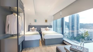 Een moderne hotelkamer met twee bedden, een bureau en een groot raam met uitzicht op de stad.