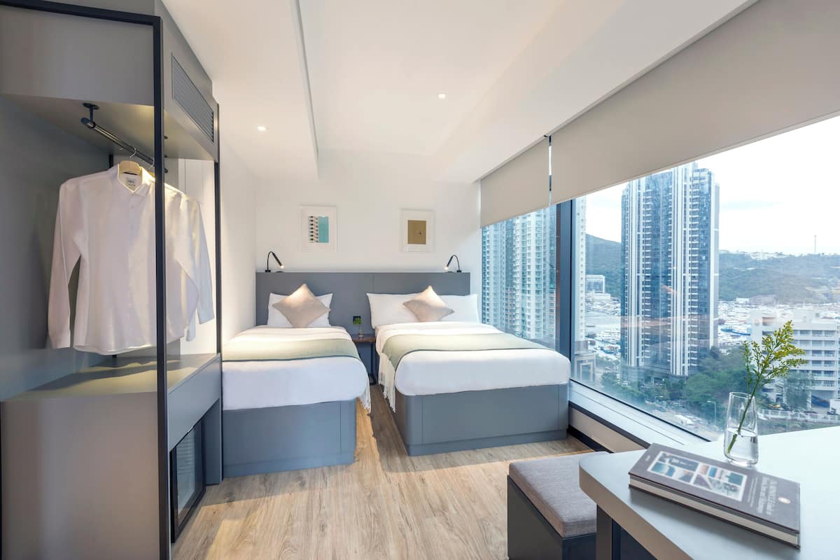 Une chambre d’hôtel moderne avec deux lits, un bureau et une grande fenêtre donnant sur la ville.