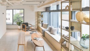 Een moderne kantoorruimte met een lange houten tafel, een bank met kussens en een boekenkast met decoratieve objecten.