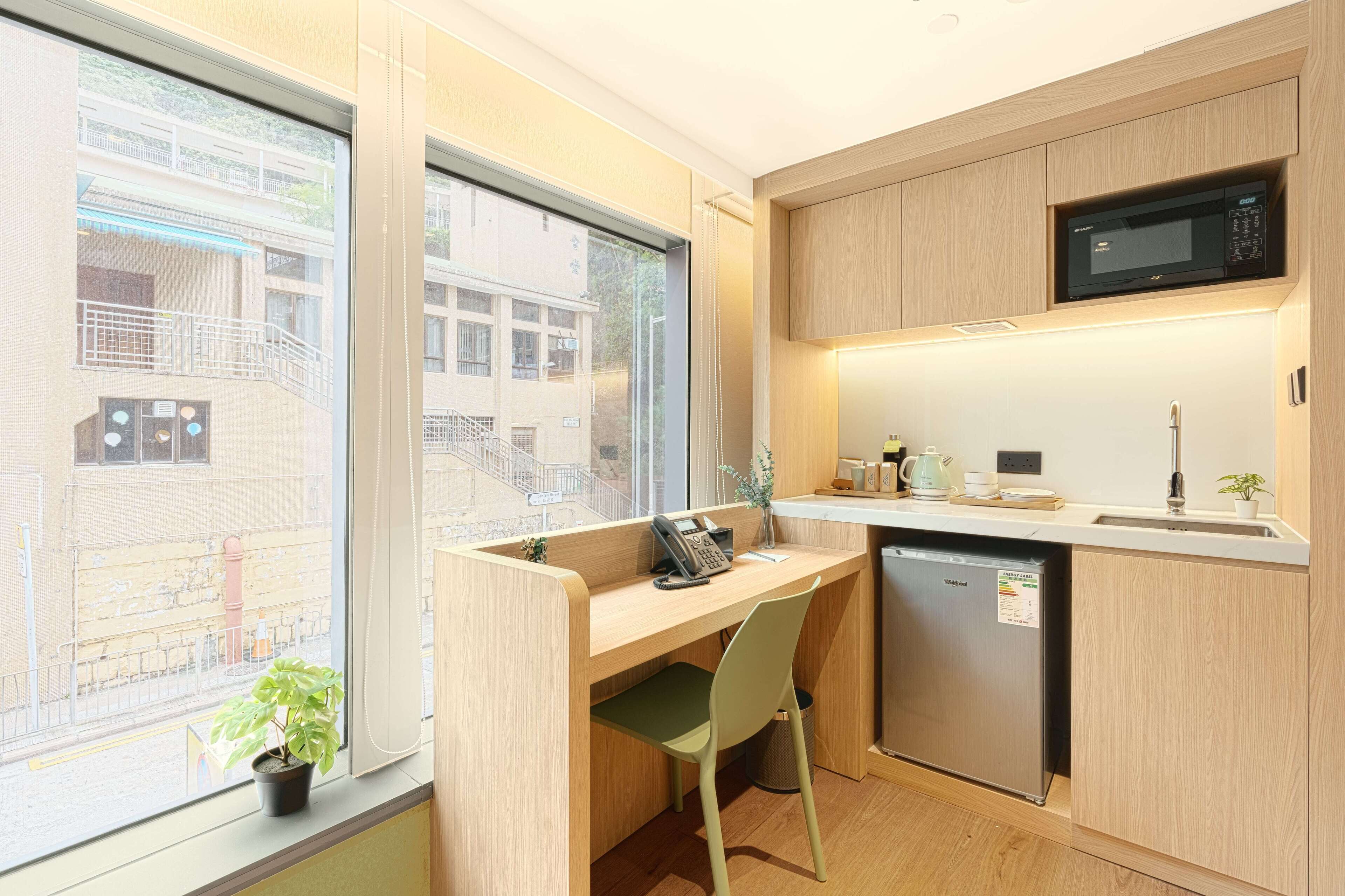 Una cocina compacta con microondas integrado, un lavamanos pequeño y ventana con vista a una zona residencial.