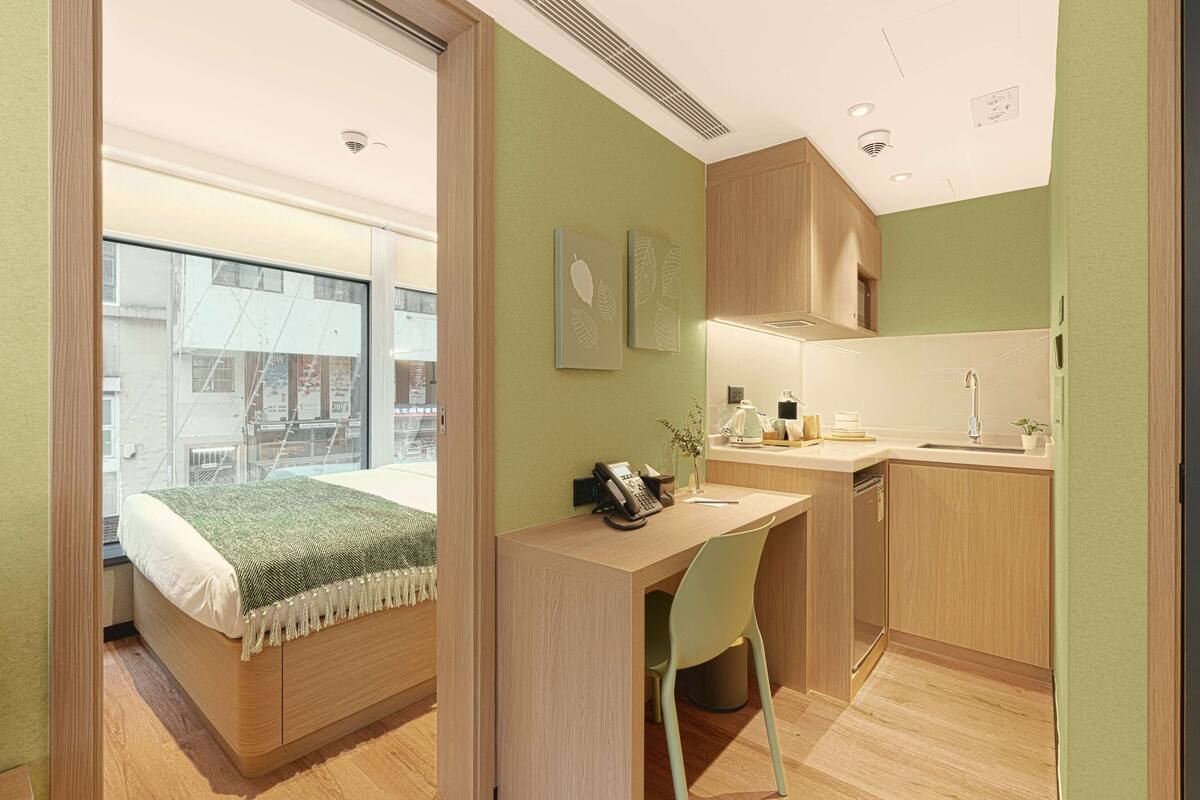 Une chambre moderne avec un lit, un bureau et une chaise, un coin cuisine et une vue par la fenêtre.