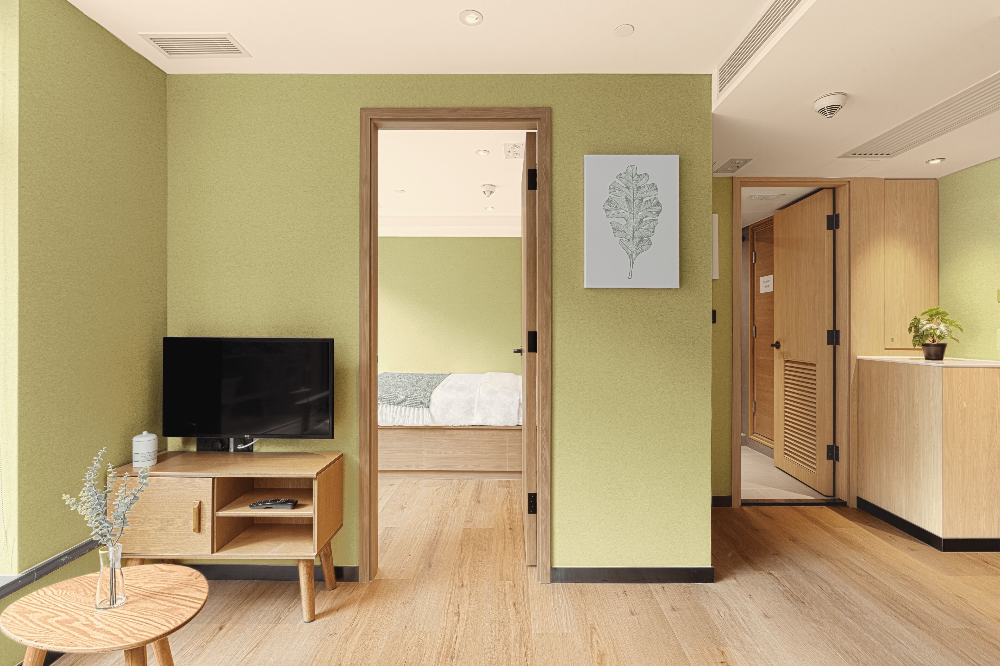 A hotel room with a bed, a TV, a small table with a vase, and a wooden cabinet.