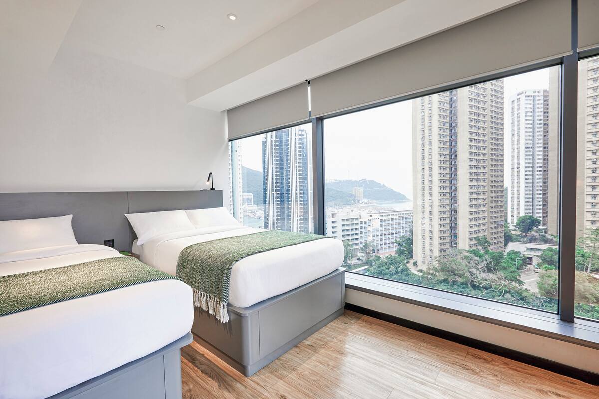 Une chambre d’hôtel moderne avec deux lits, une grande fenêtre donnant sur la ville et un plancher en bois.