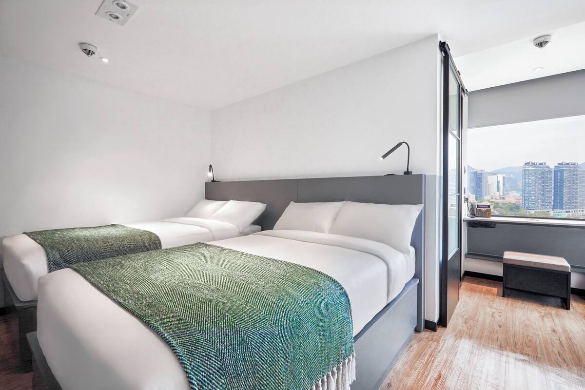 Une chambre d’hôtel moderne avec deux lits, une vue sur la ville et un banc près de la fenêtre.