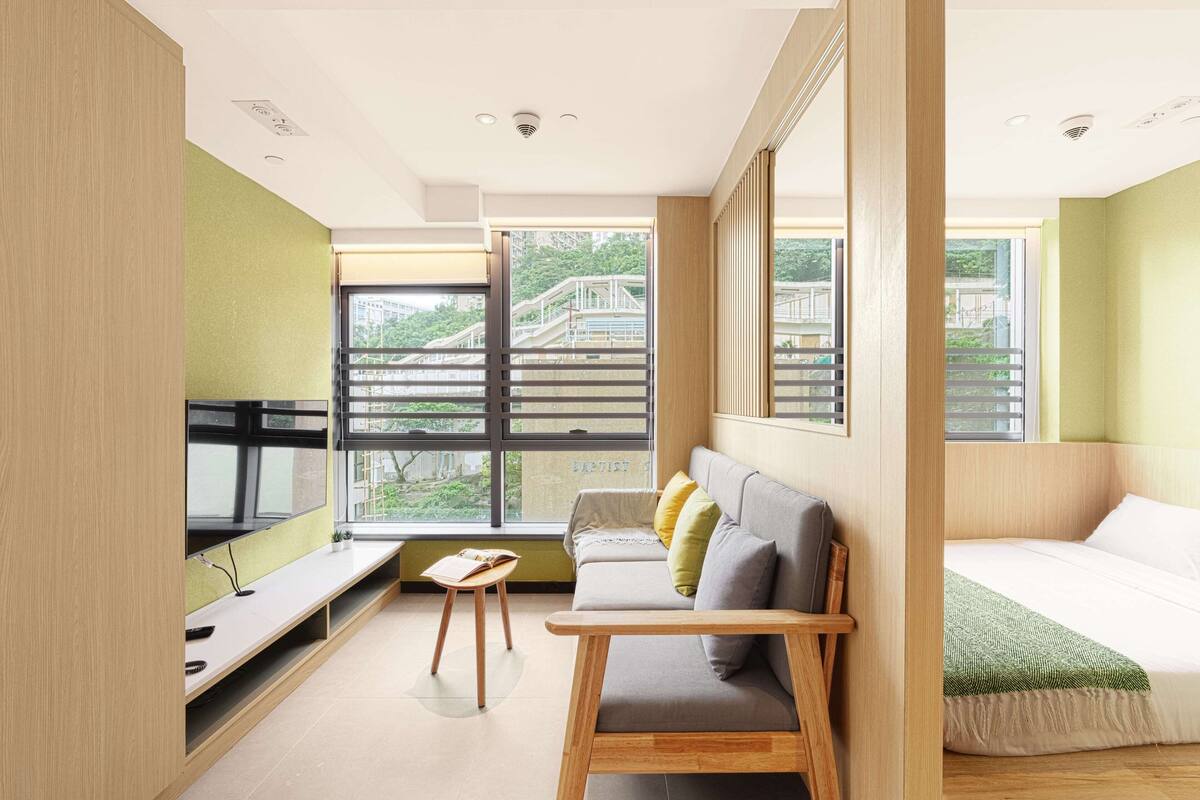 Une chambre moderne équipée d’un lit, d’un canapé, d’une petite table et de grandes fenêtres donnant sur un bâtiment à l’extérieur.