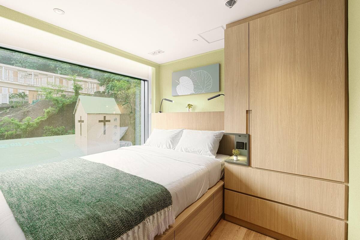 Une chambre à coucher comprenant un lit, une table de chevet, une armoire, une fenêtre et une œuvre d’art accrochée au mur.