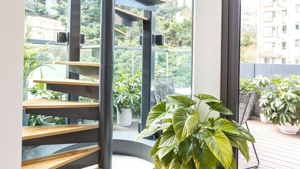 Een moderne spiraaltrap met houten treden en metalen leuningen, die uitkomt op een balkon met plantenpotten.