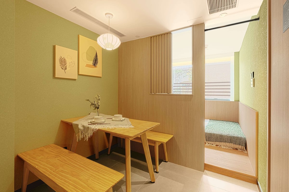 Une petite pièce chaleureuse, avec une table et des bancs en bois, une fenêtre donnant sur un beau paysage et deux tableaux encadrés accrochés au mur.