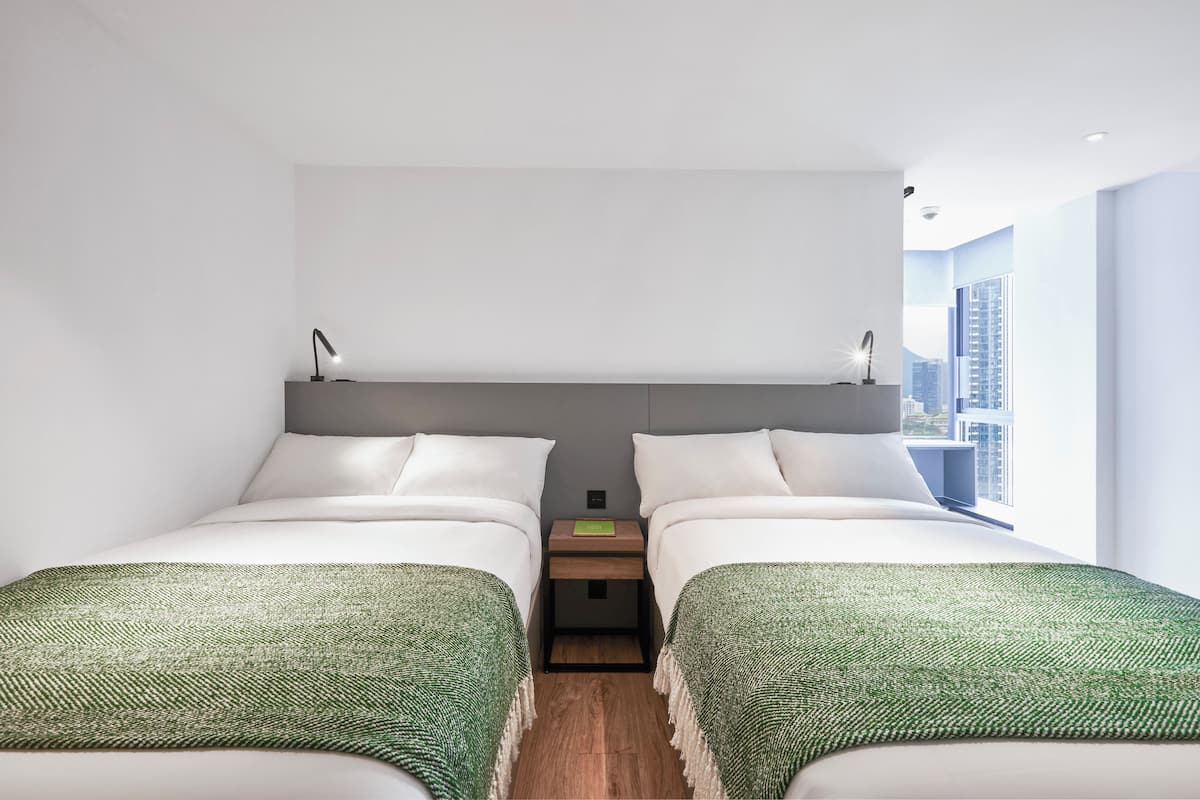 Une chambre d’hôtel moderne avec deux lits, une table de chevet et une vue sur la ville.