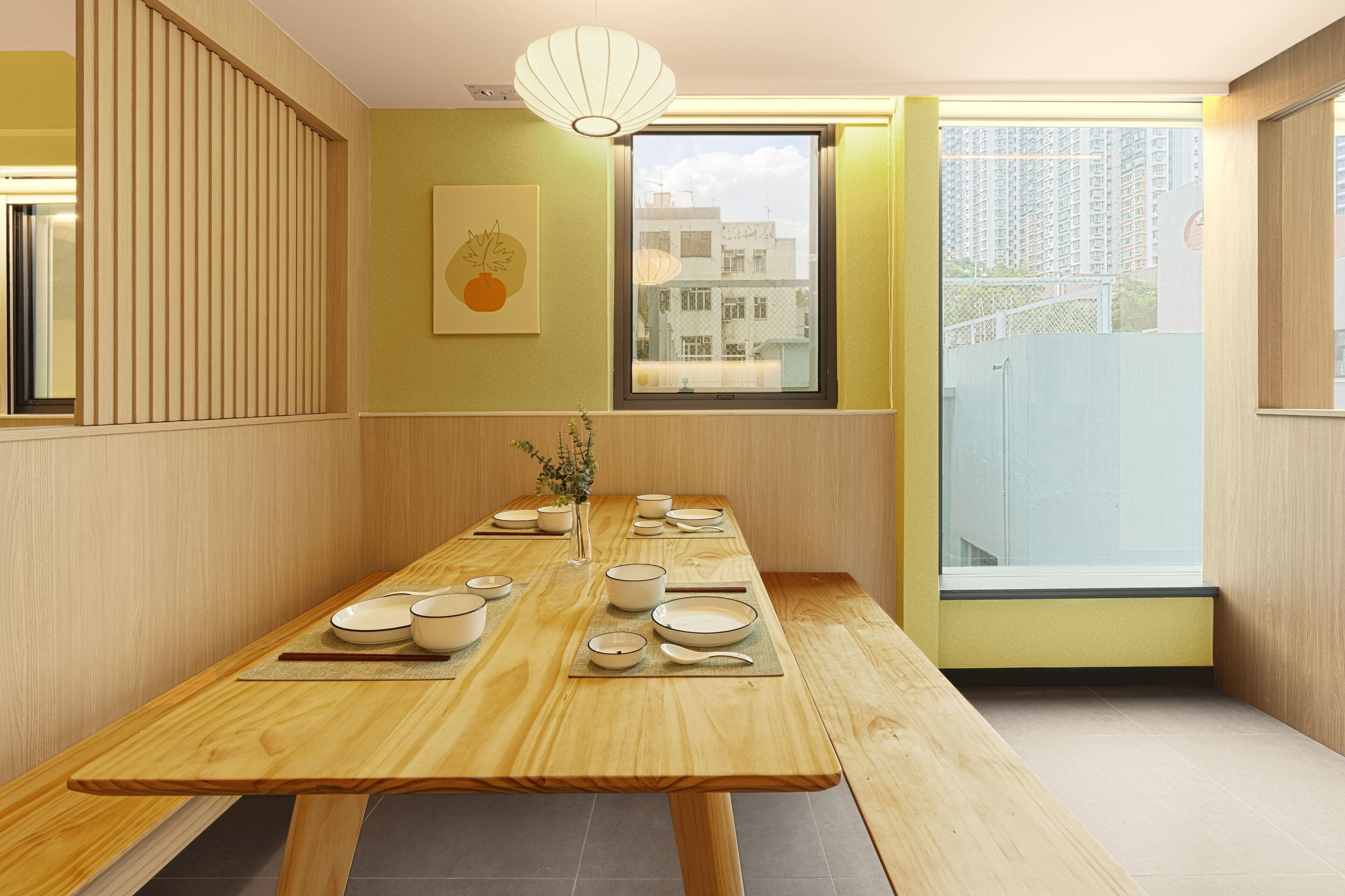 A dining area with a wooden table set for a meal, a vase with flowers, and a window with a view of buildings.