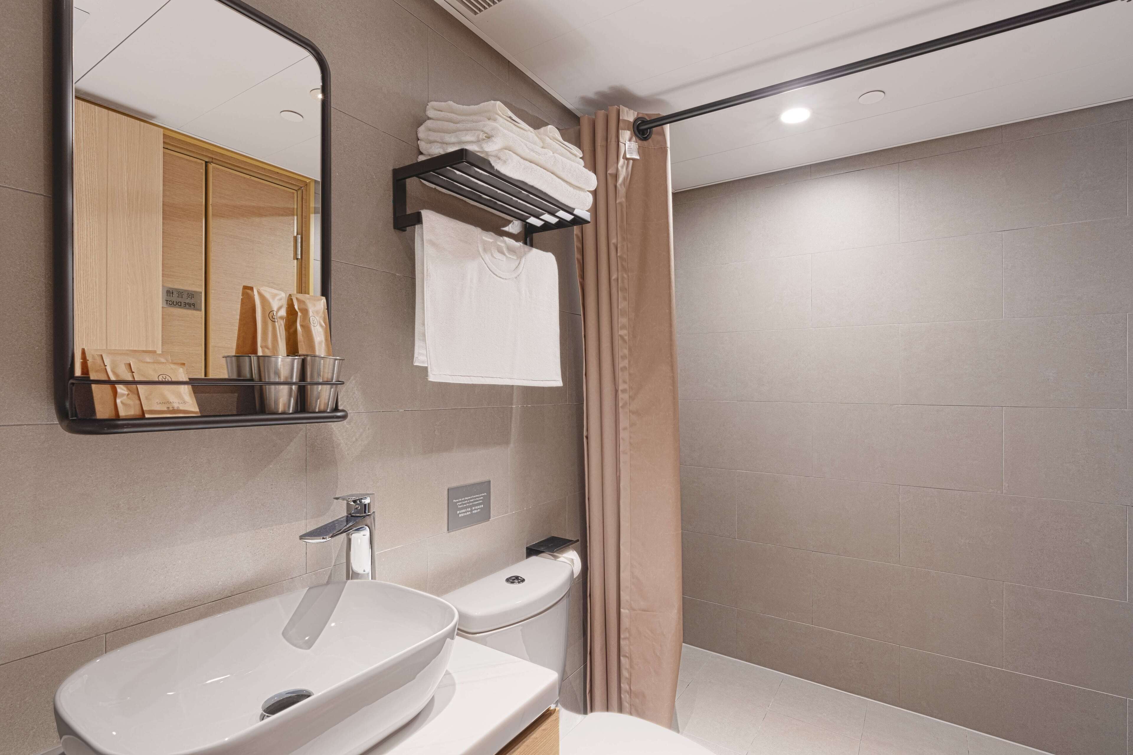 A modern bathroom with a large mirror, a sink, a toilet, and a shower area.