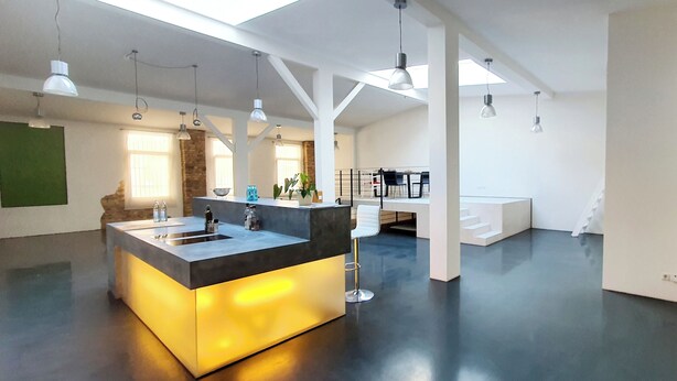 A modern kitchen with a central island, pendant lighting, and a staircase leading to an upper level. - Loft für Besondere Momente (Mannheim)