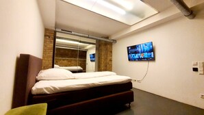 A modern bedroom with a bed, a TV mounted on the wall, and a skylight above. - Loft für Besondere Momente (Mannheim)
