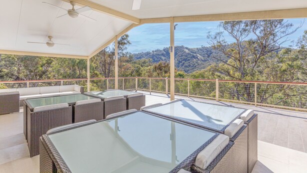 A covered outdoor area with a pool table, seating, and a scenic view of trees and hills.