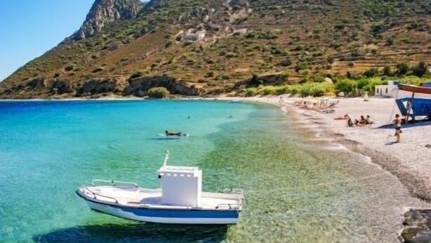 Ein Boot liegt vor einem Strand mit klarem Wasser und einer Bergkulisse.
