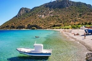 Een boot afgemeerd nabij een strand met helder water en een bergachtige achtergrond.