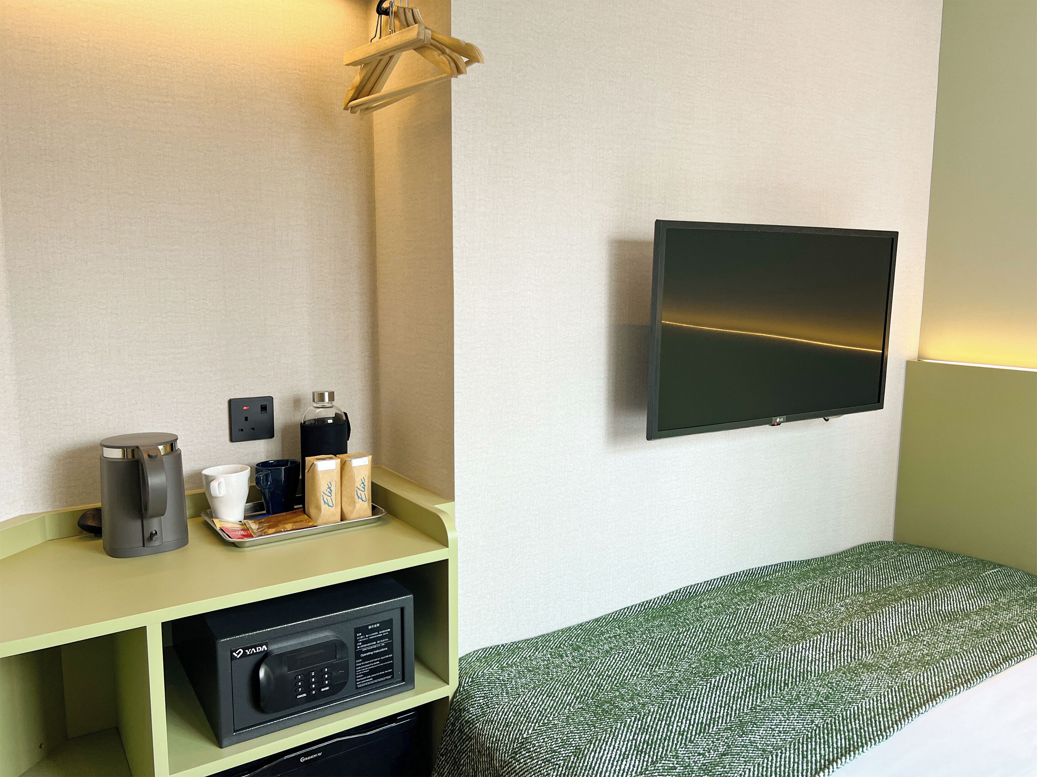 A hotel room with a flat-screen TV mounted on the wall, a coffee maker, a kettle, and a tray with bags and cups on the counter.