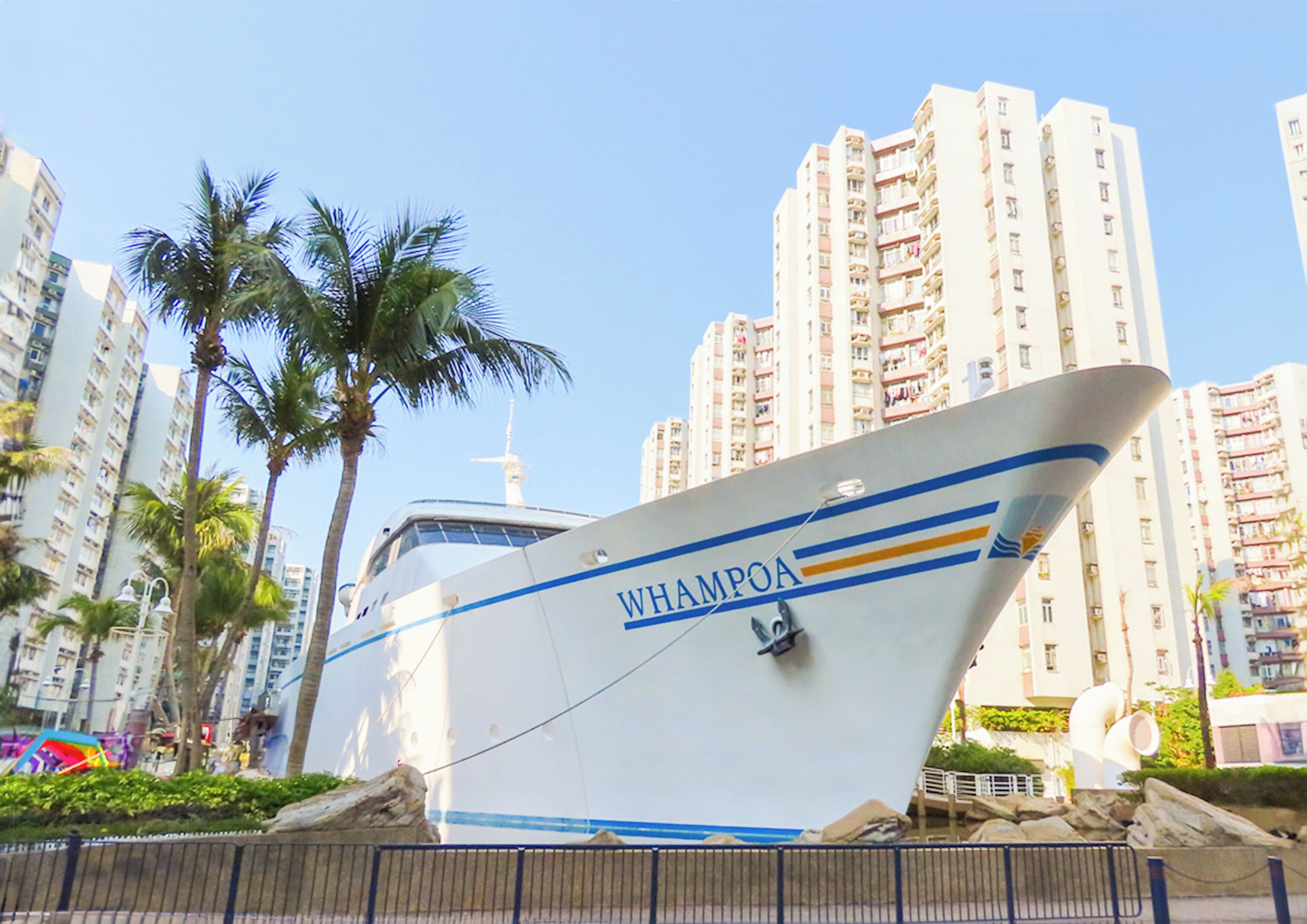 A large yacht named WHAMPOA docked in a marina with high-rise buildings and palm trees in the background.
