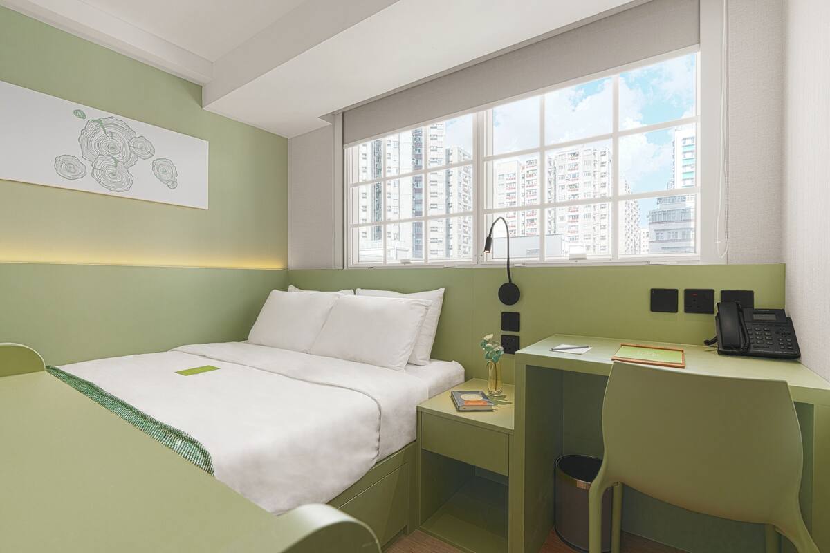 A compact hotel room with a bed, a desk with a phone, and a window with a city view.