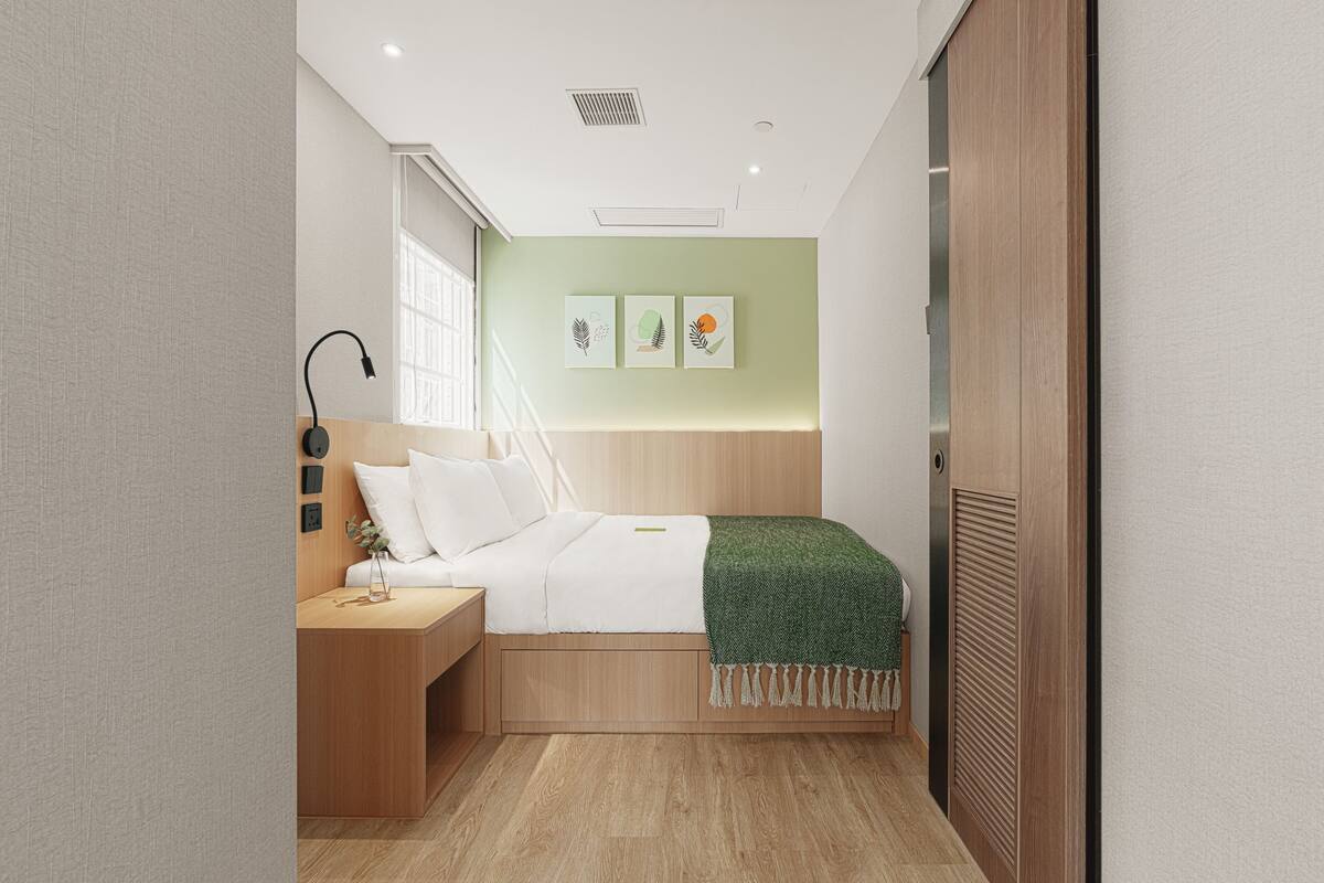 A modern bedroom with a wooden bed, a bedside table, a nightstand, and a wall-mounted lamp.