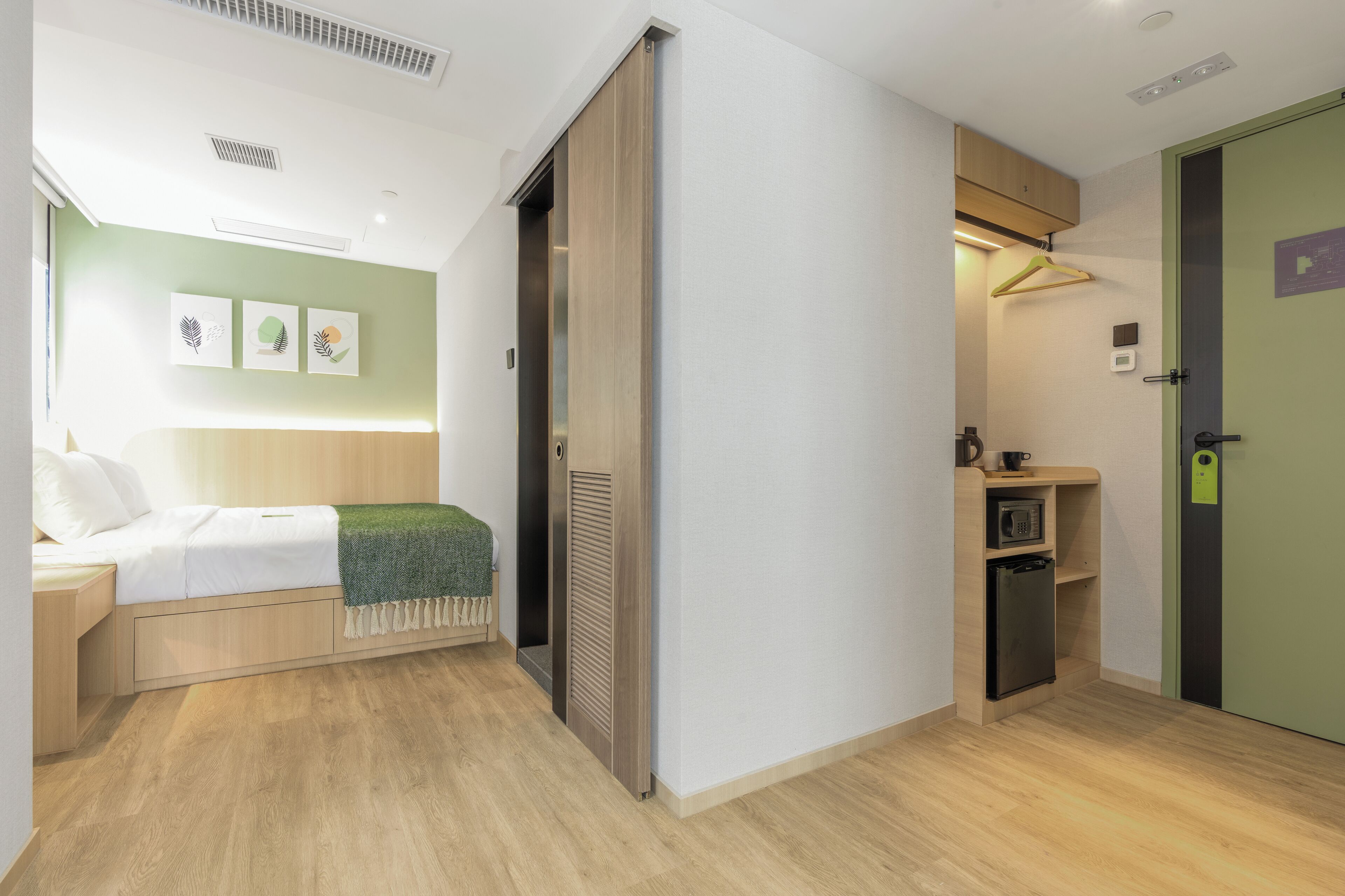 Habitación de hotel compacta con cama, un escritorio pequeño, un microondas y una puerta verde.