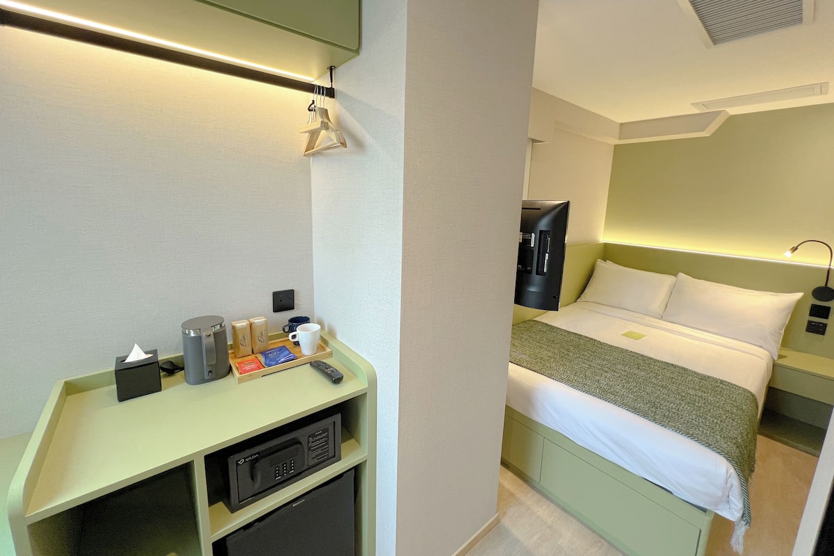 A hotel room with a bed, bedside table, and a desk with a computer and other items.