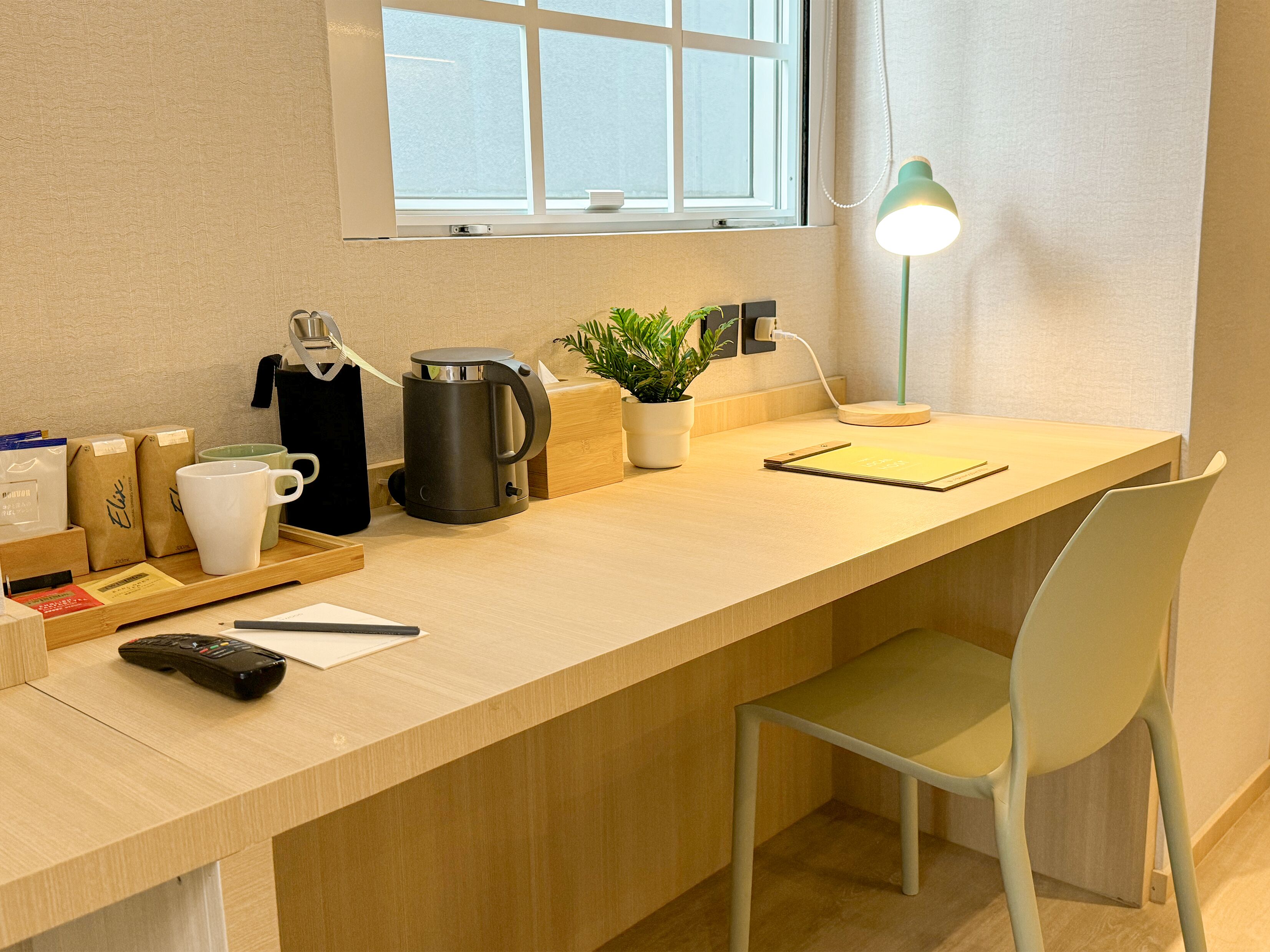 A modern workspace with a wooden desk, a laptop, a coffee maker, a potted plant, and a desk lamp.