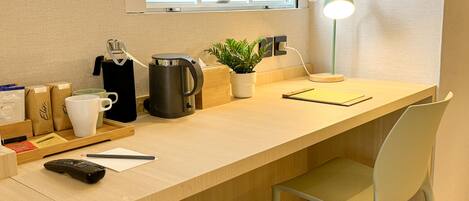 A modern workspace with a wooden desk, a laptop, a coffee maker, a potted plant, and a desk lamp.