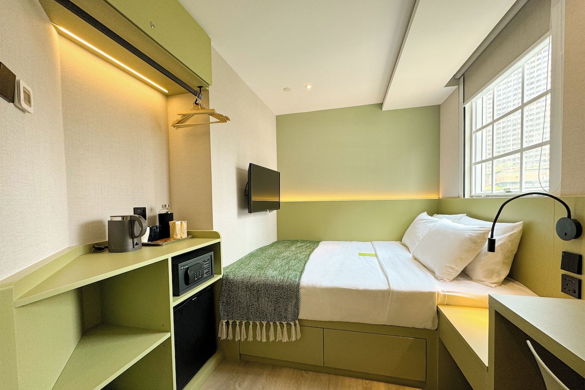 A compact hotel room with a bed, bedside table, TV, and a small desk with a computer.