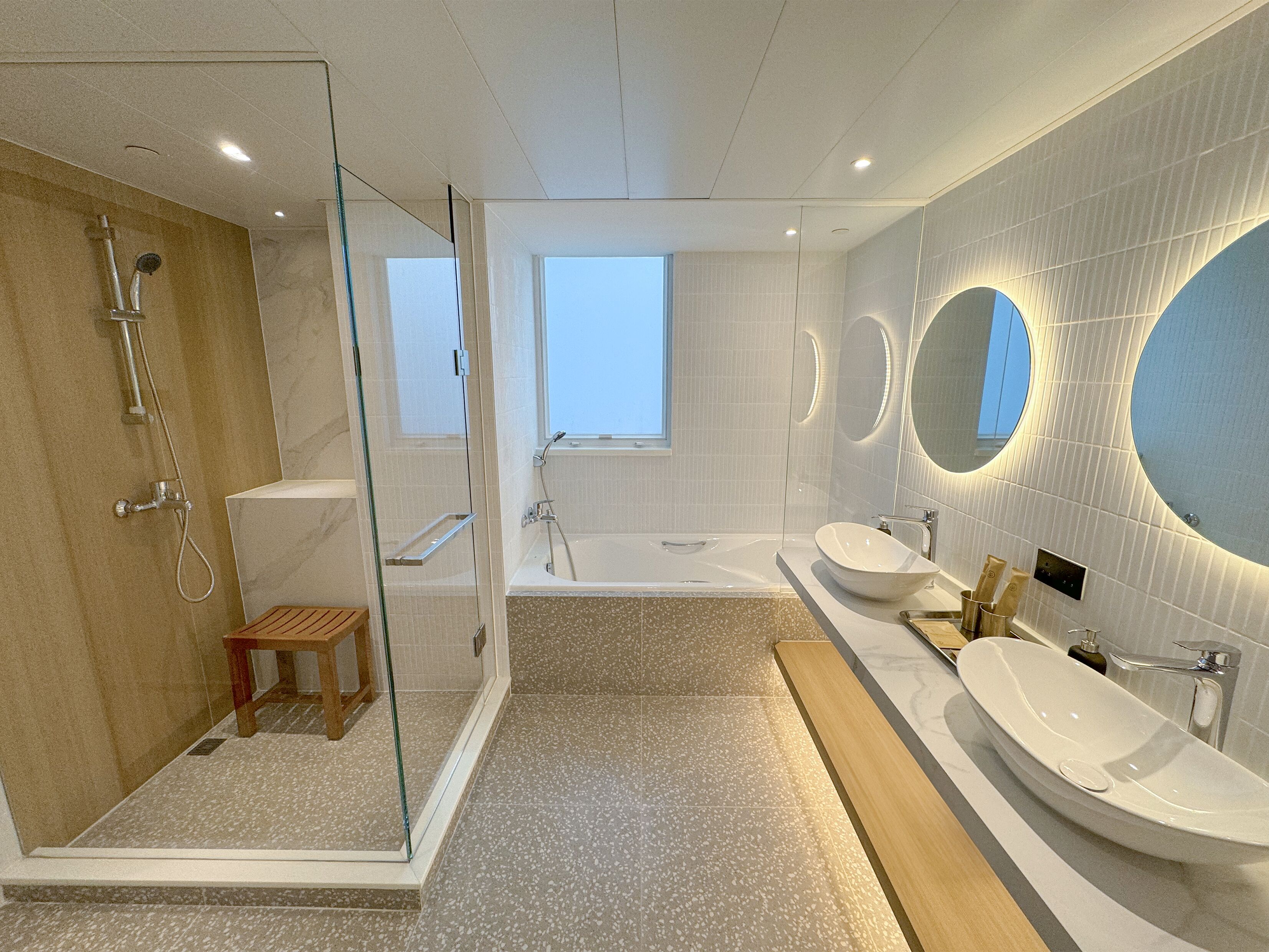A modern bathroom with a glass-enclosed shower, a bathtub, and two sinks.