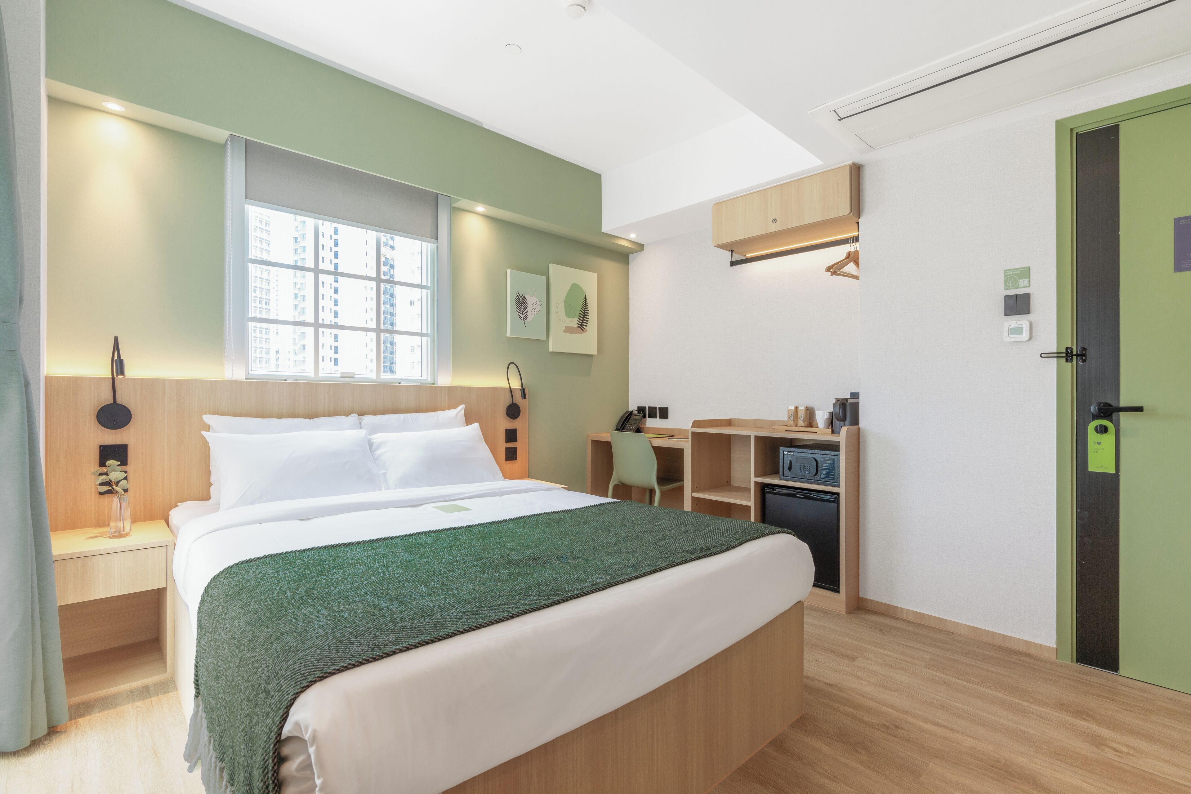 A hotel room with a bed, a desk, a chair, a small kitchenette, and a green door.