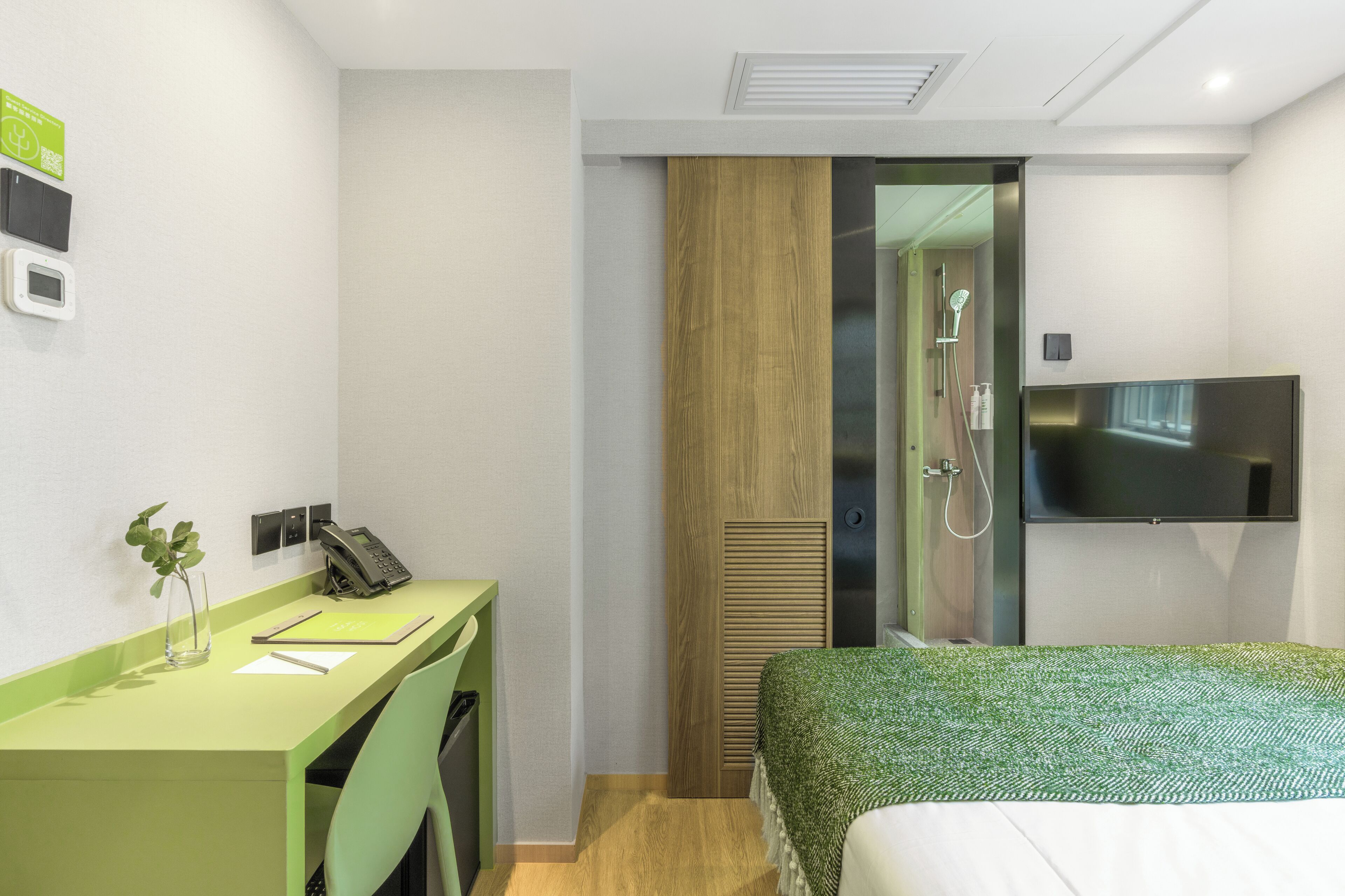 A hotel room with a desk, a bed, a TV, and a shower.