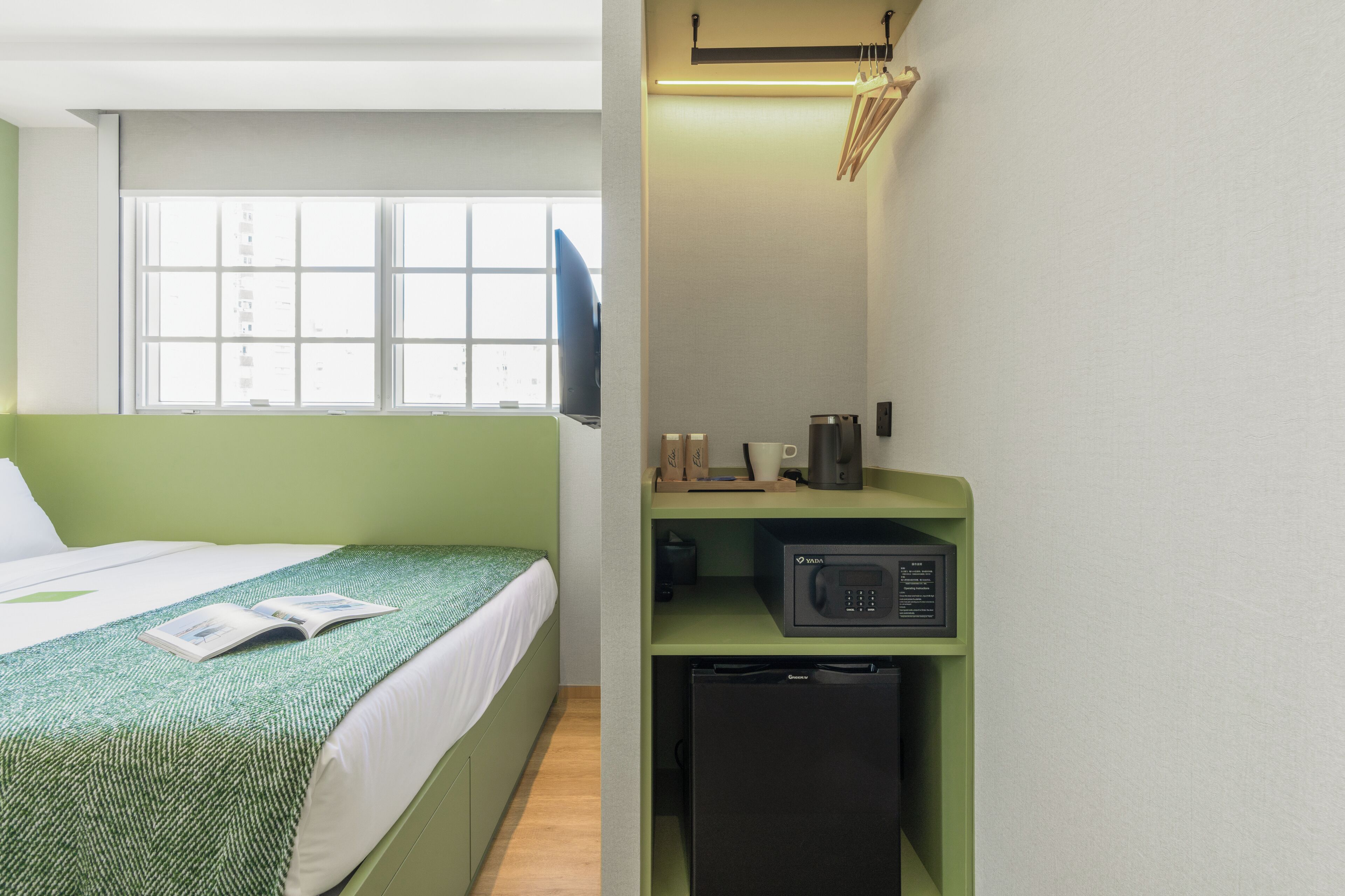 A compact hotel room with a bed, a small kitchenette, a microwave, and a window with blinds.