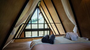 Un dormitori sota els teulats acollidor, de forma triangular, amb un llit, tovalloles arremolinades i cortines primes.