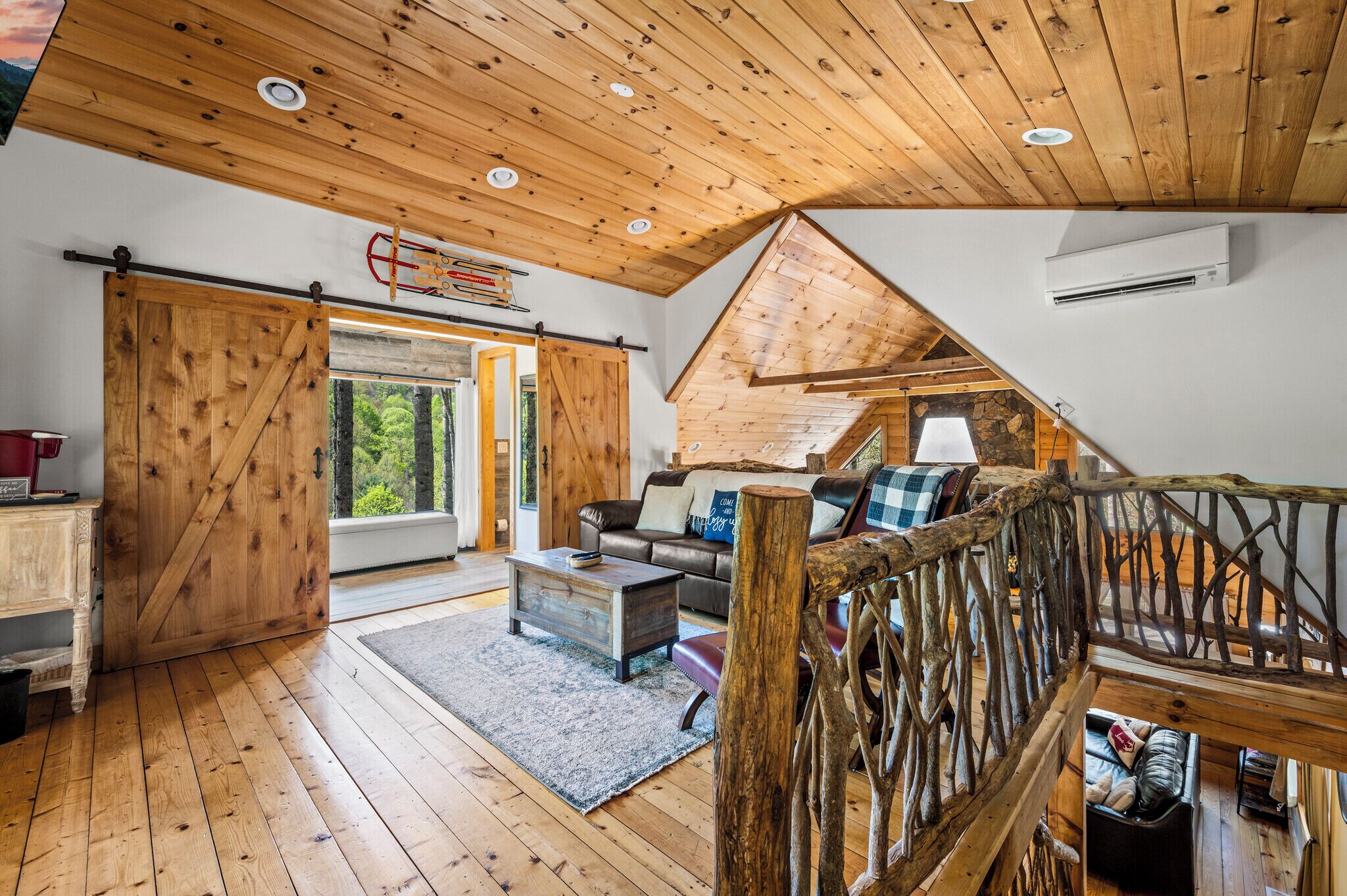 Een rustiek houten interieur met houten vloeren, een slaapvide met schuine wanden, een grote schuifdeur en een gezellige zithoek met een bank en kussens.