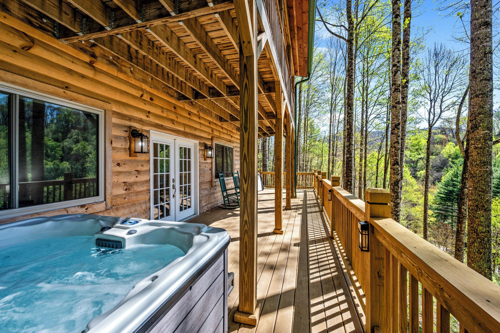 Une terrasse en bois avec un jacuzzi, des rampes en bois et une vue sur une forêt.