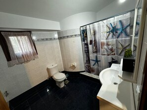 A bathroom with a toilet, sink, and shower curtain with starfish and seashells. - Moonbeam Townhouse Skiathos (Skiathos)