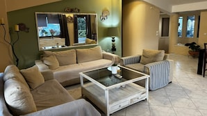 A living room with a beige sofa, a striped armchair, and a glass coffee table. - Moonbeam Townhouse Skiathos (Skiathos)