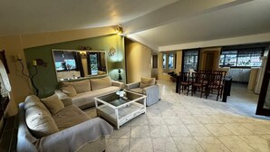 A spacious living room with a large sofa, a coffee table, and a dining area with wooden chairs. - Moonbeam Townhouse Skiathos (Skiathos)