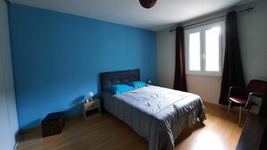 Ein Schlafzimmer mit einem Bett, einem Nachttisch, einem Sessel und einem Fenster mit Vorhängen.