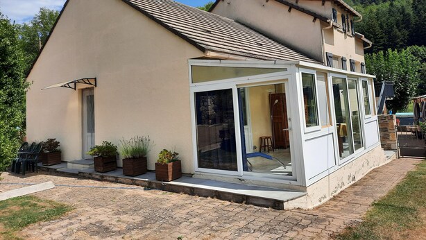 Ein zweistöckiges Haus mit Satteldach, einer Veranda mit Glasüren und einem kleinen Garten mit Topfpflanzen.
