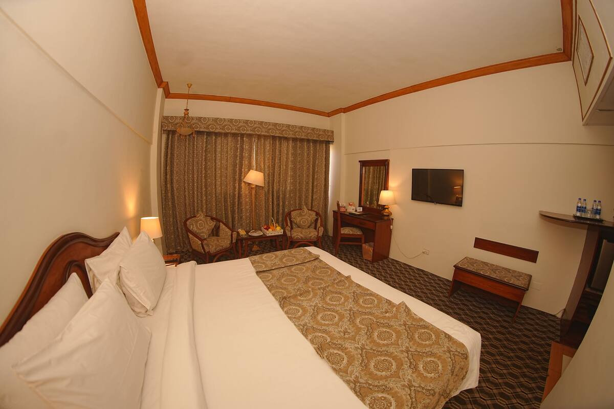 A hotel room with a bed, a desk, a chair, a lamp, a television, and a small table with a mirror.