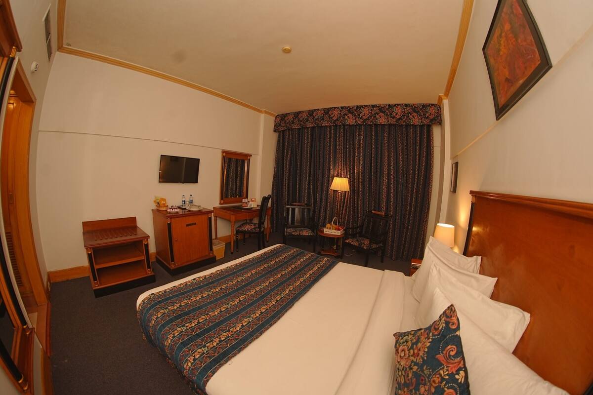 A hotel room with a bed, desk, chair, and a television on the wall.