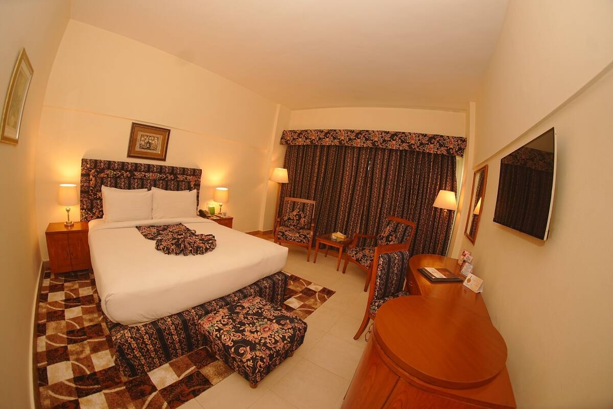 A hotel room with a large bed, a desk, two chairs, a small table, and a mirror.