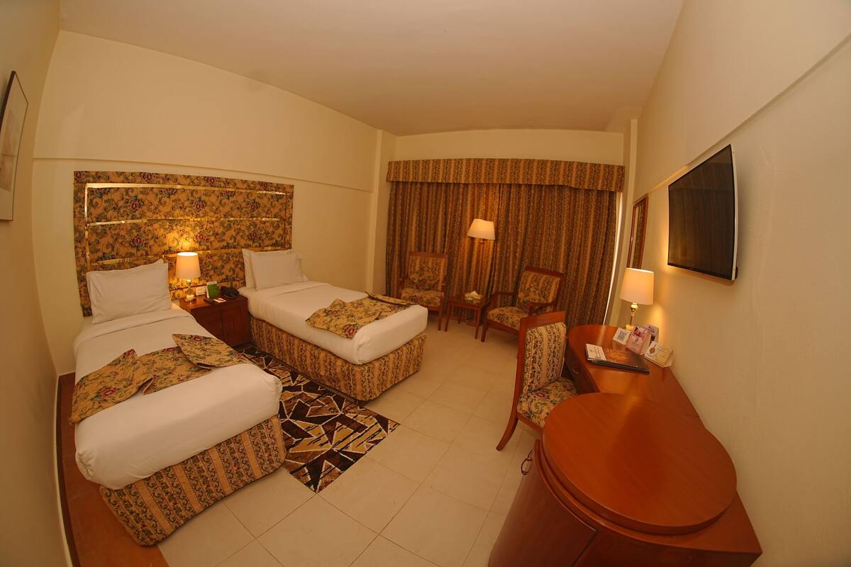 A hotel room with two beds, a desk, a chair, a TV, and a window with curtains.