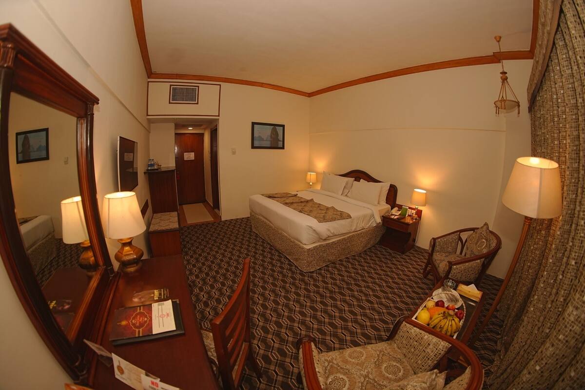 A hotel room with a bed, bedside table, lamp, chair, and a small table with fruit.