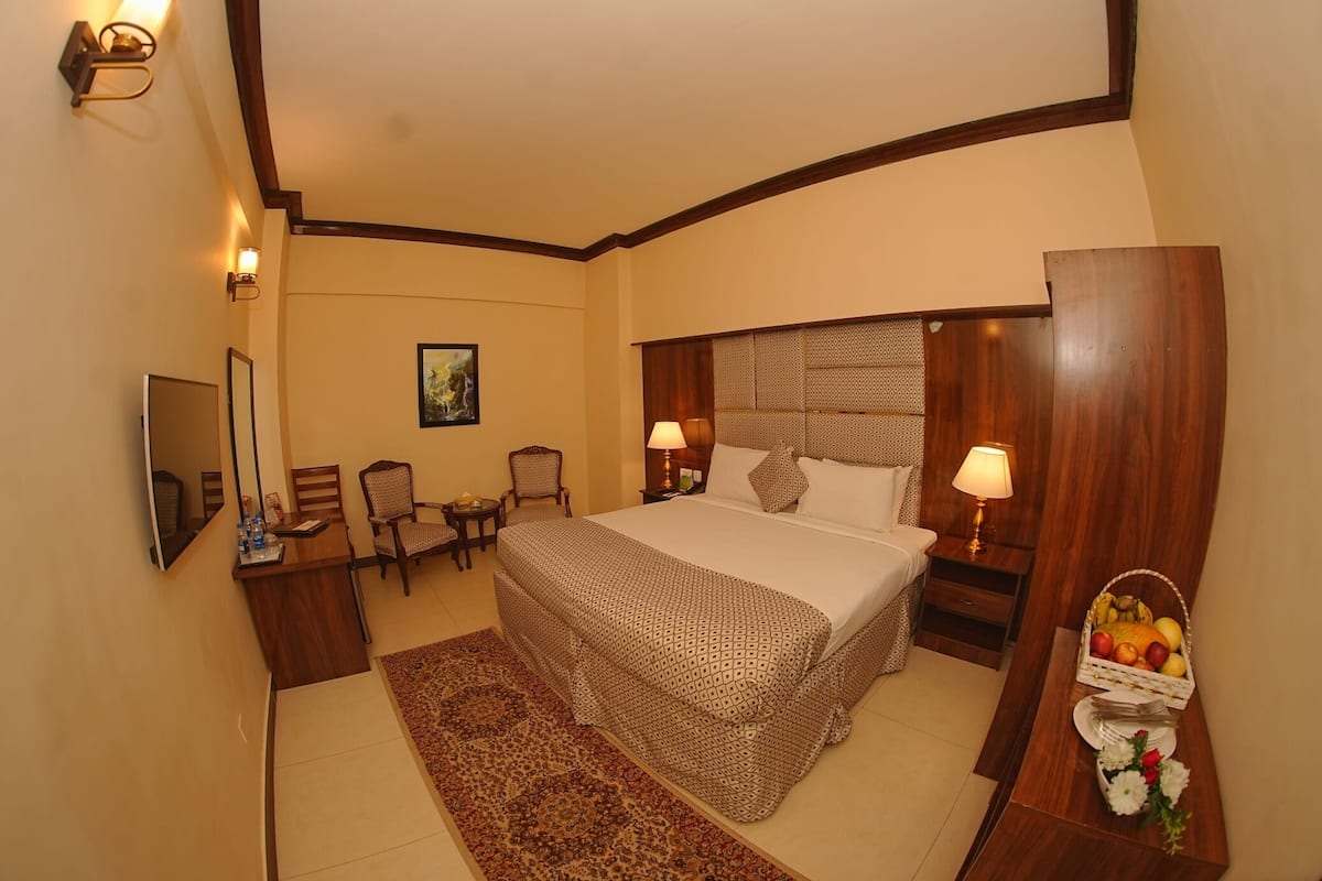 A hotel room with a large bed, bedside lamps, a desk with a chair, a small table, and a fruit basket.