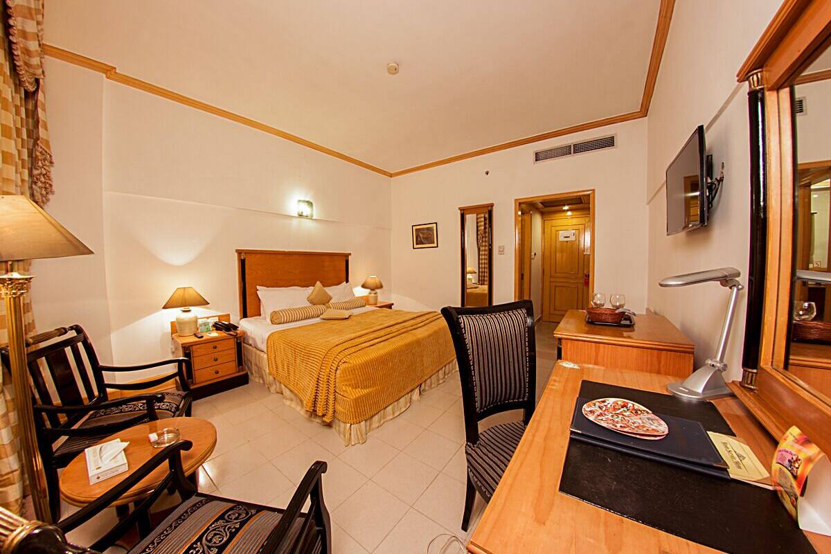 A hotel room with a bed, a desk, a chair, a TV, and a lamp.
