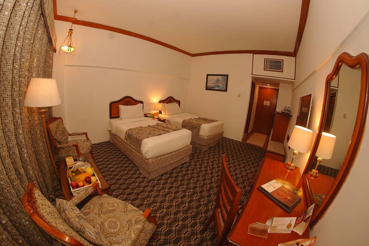A hotel room with two beds, a dining table, a chair, a mirror, and a chandelier.