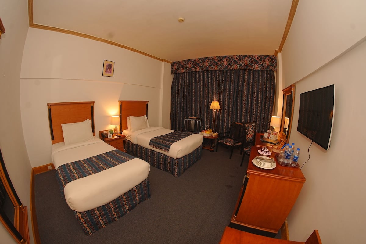 A hotel room with two beds, a desk, a chair, a TV, and a window with curtains.